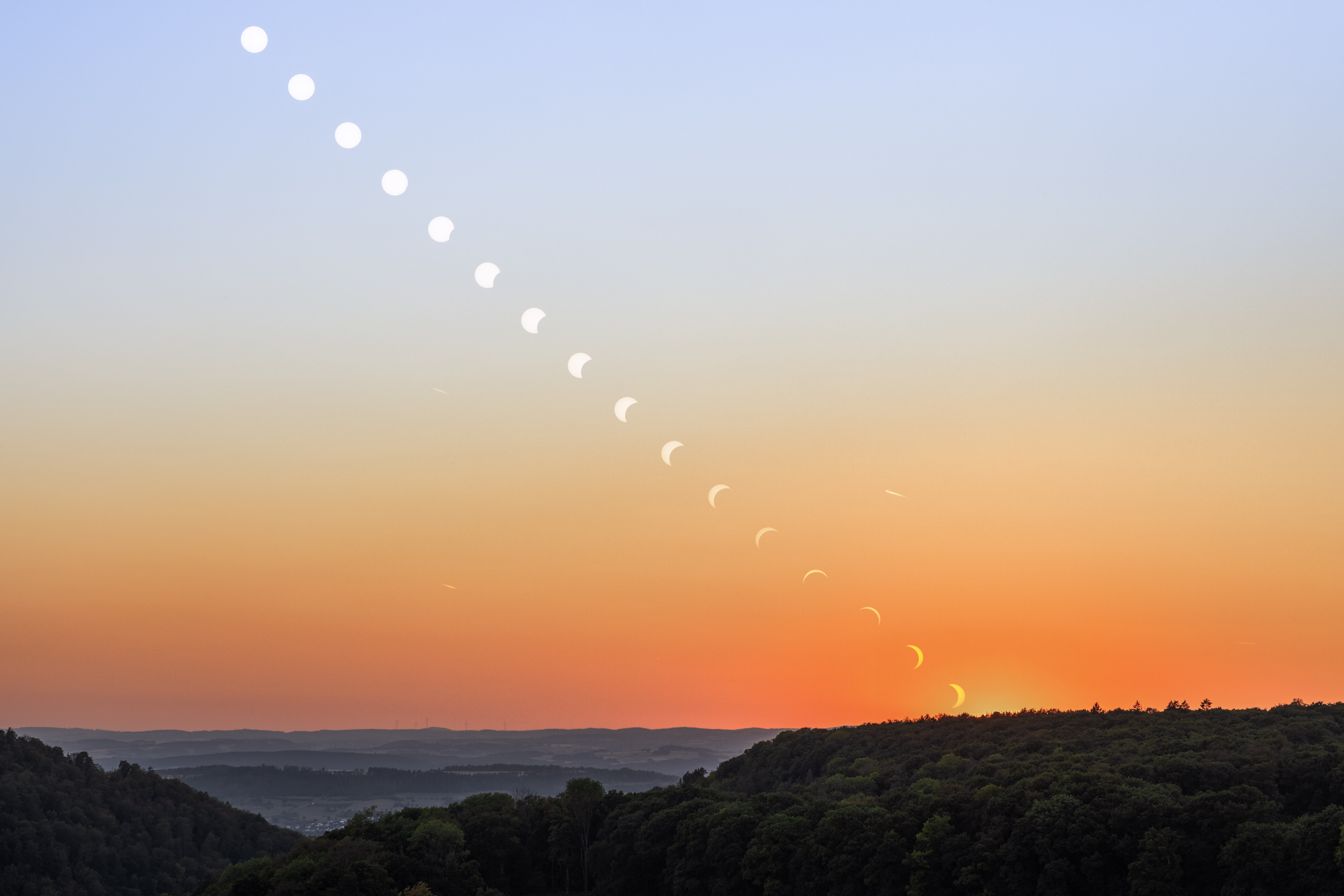 Weitwinkel-Übersicht des Finsternisverlaufs, die schmaler werdende Sonnensichel wandert zum Horizont und geht unter